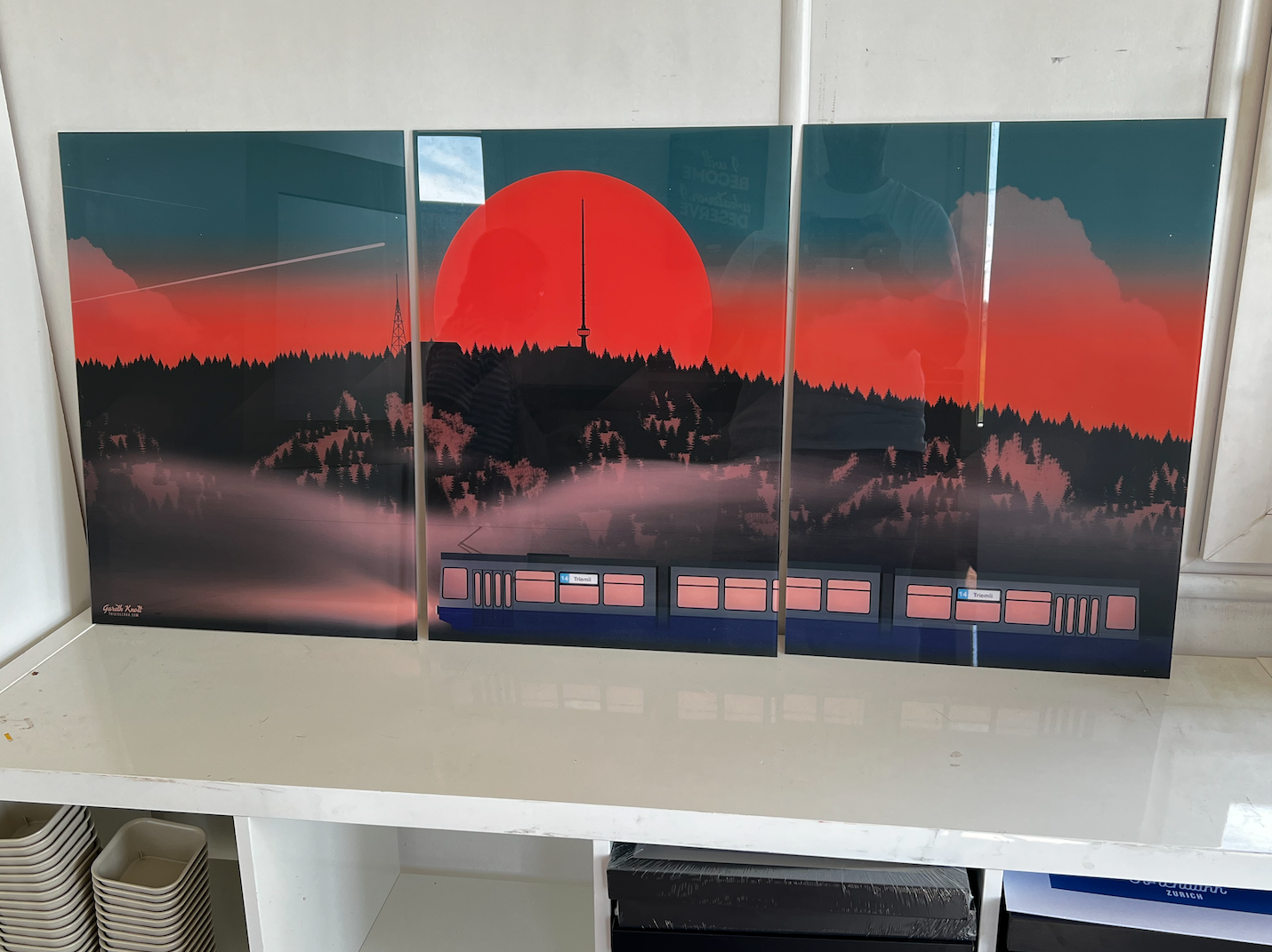 A three-panel wall art print depicting a red sunset behind the Uetliberg along the bottom, has tram 14 Triemli.