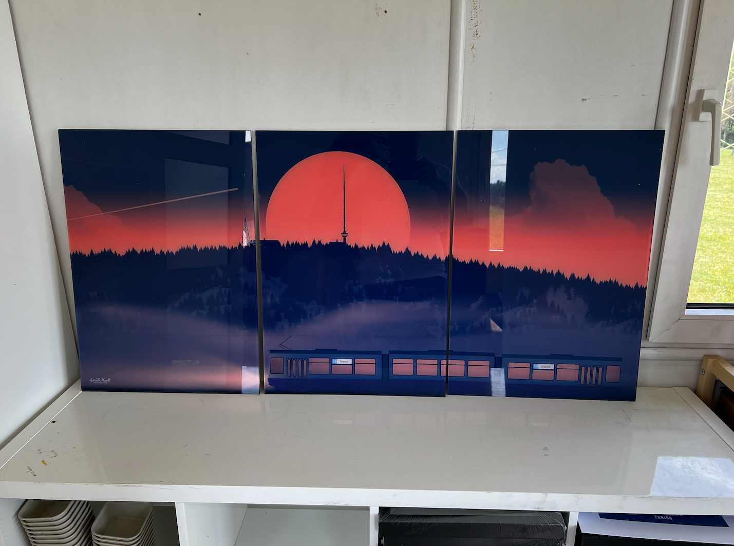 A three-panel wall art print depicting a pink and blue sunset behind the Uetliberg along the bottom, has tram 14 Triemli.